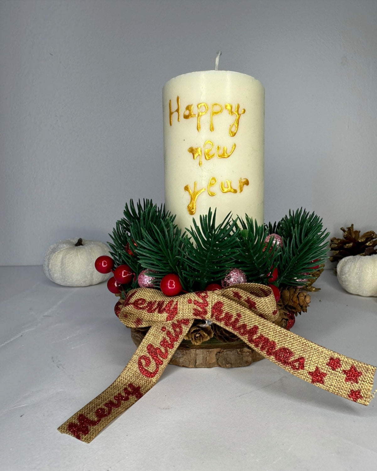 Χριστουγεννιάτικη σύνθεση με ιβουάρ κερί Happy New Year, πράσινα κλαδάκια, κουκουνάρια και γιορτινό φιόγκο