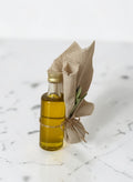 ELAIOPHOS miniature olive oil bottle with burlap accent and twine, featuring golden oil and a sprig of greenery.
