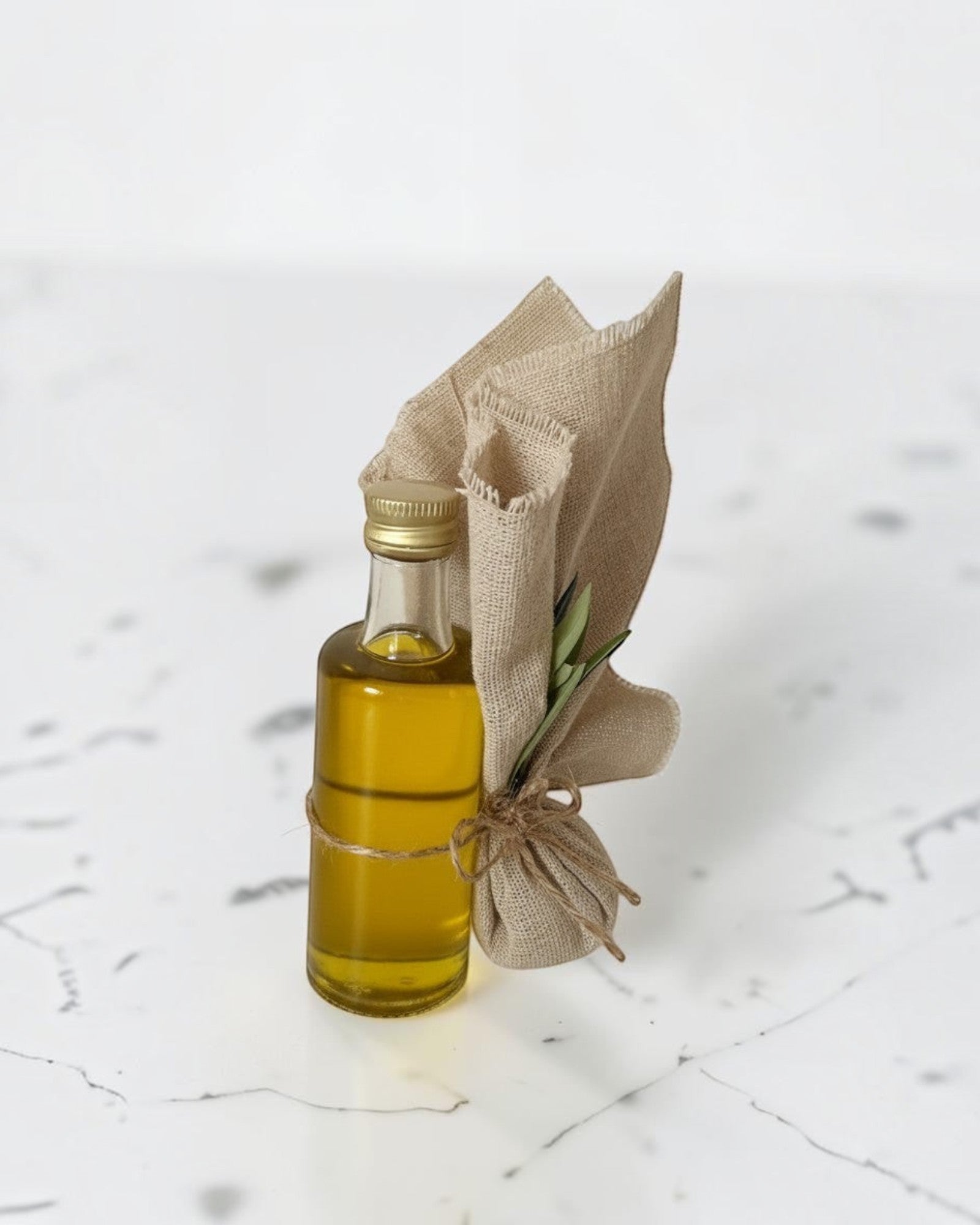ELAIOPHOS miniature olive oil bottle with burlap accent and twine, featuring golden oil and a sprig of greenery.